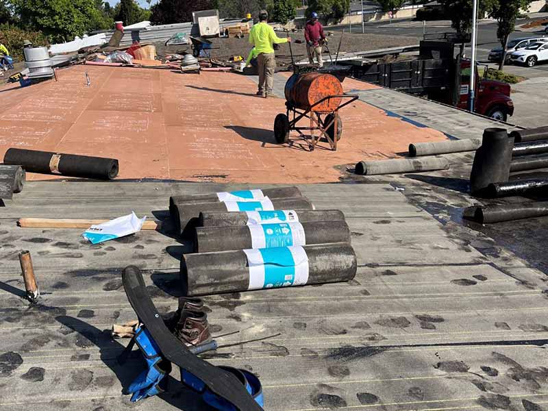 Henris Roofing Company workers installing new rubber membranes on a sloped commercial roof
