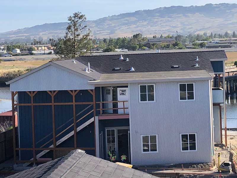 Front view of a small, two-story home with metal siding, black shingles on the roof, and the California mountains in the background