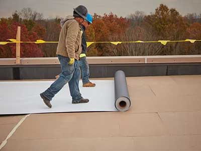 Two workers rolling out a GAF white TPO sheet
