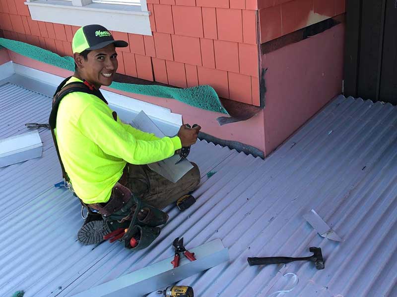 Henris Roofing Company worker smiling at the camera as they cut up a metal panel for a metal roof they are installing